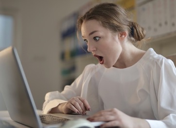 Woman looking at computer screen and appearing shocked.