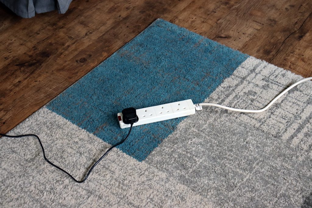 Picture of a power cable plugged into an extension socket across a rug.